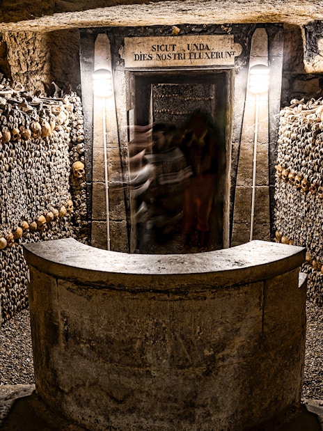 Underground catacombs with walls lined with human skulls and bones.