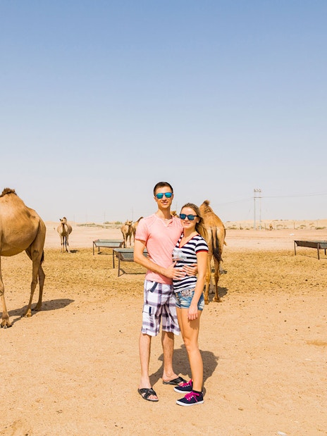 Couple standing near camels in Dubai desert during safari tour.