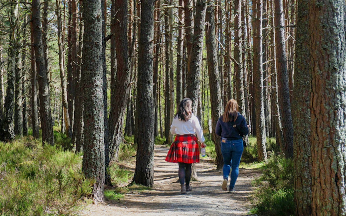 Two people walking through a forest in the Scottish Highlands.