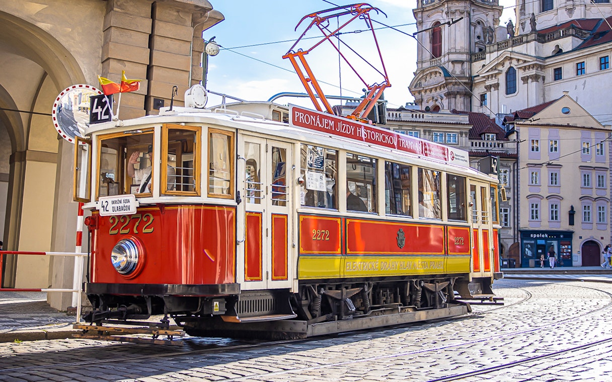 Historic red tram on cobblestone street during Prague hop-on hop-off tour.