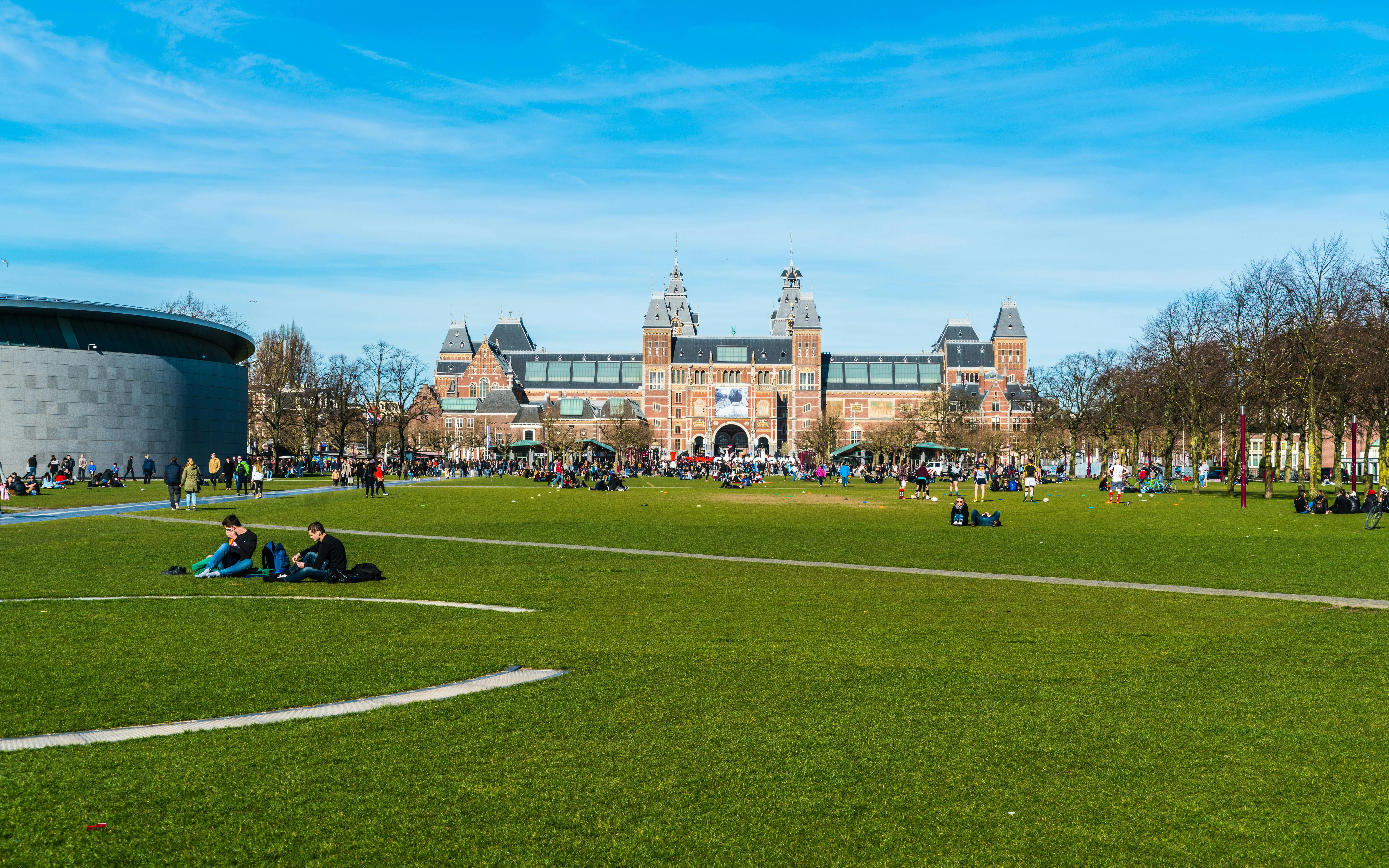 People relaxing on the grass at Museumplein with the Rijksmuseum in the background.