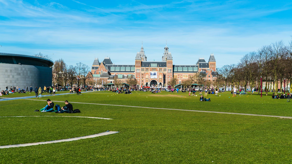 People relaxing on the grass at Museumplein with the Rijksmuseum in the background.