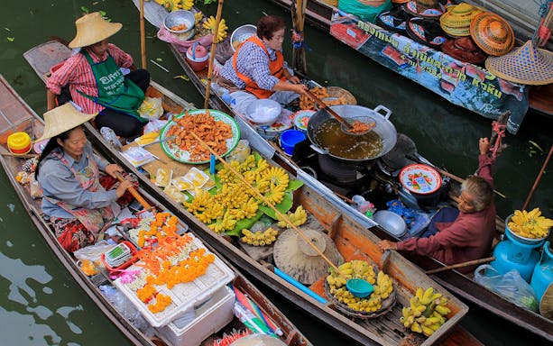 Floating market vendors selling fruits and fried snacks in Bangkok, Thailand.
