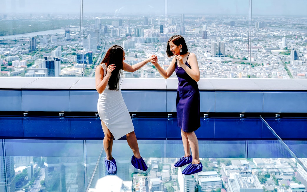 Friends enjoying the glass floor at Mahanakhon SkyWalk, Bangkok, Thailand.