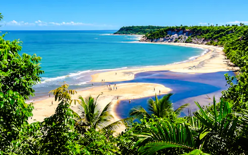 Caraíva beach with river meeting ocean, surrounded by lush greenery, Porto Seguro, Brazil.