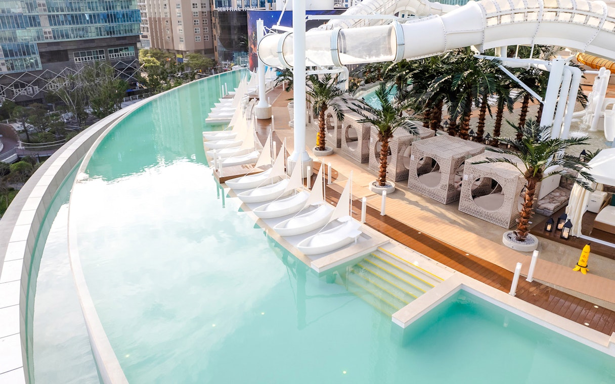 Rooftop infinity pool with sail-shaped loungers, cabanas, and waterslide at Club D Oasis.