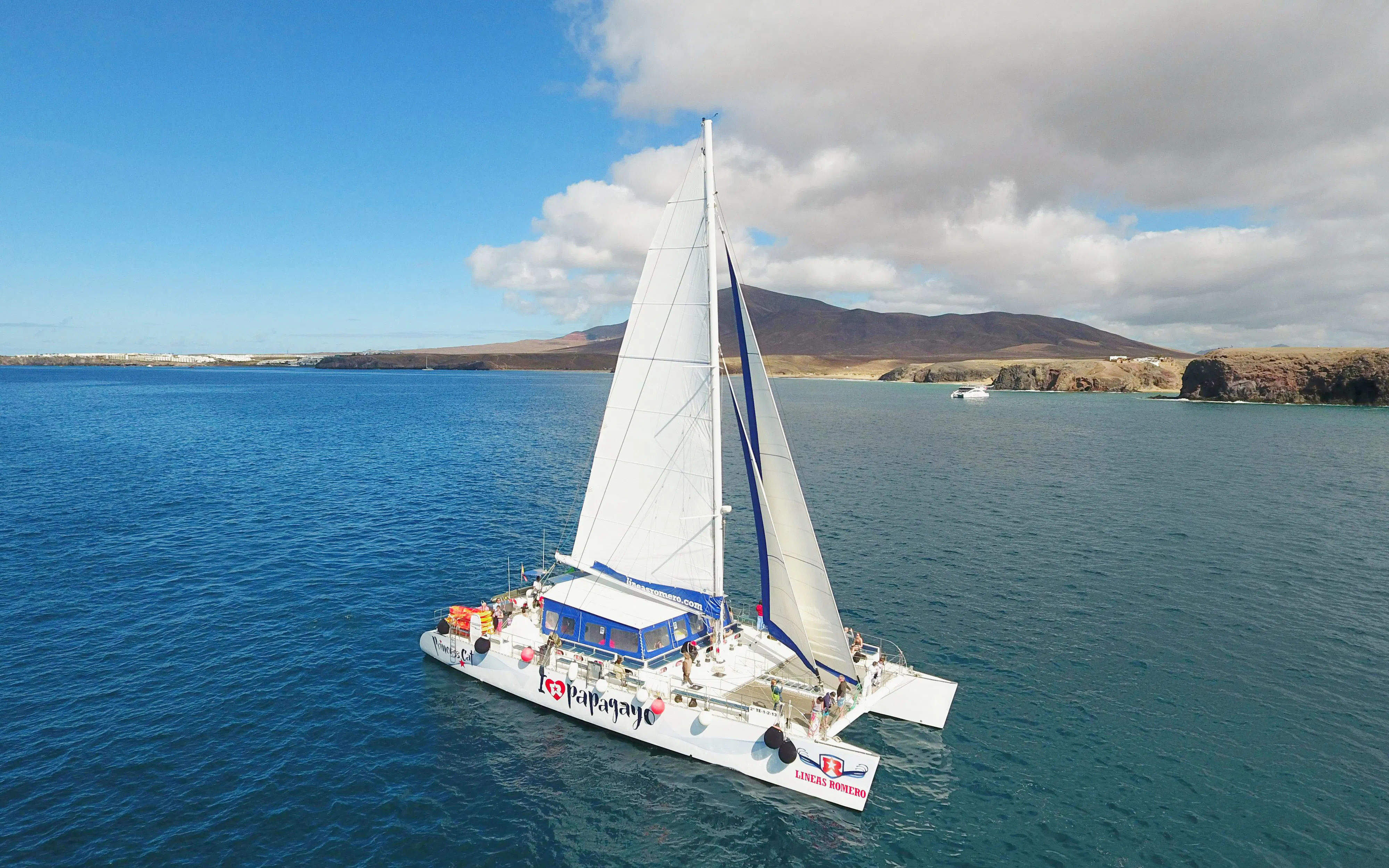 Catamaran sailing near Papagayo Beaches, Lanzarote, with distant cliffs and clear blue water.