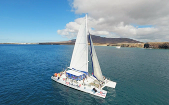 Catamaran sailing near Papagayo Beaches, Lanzarote, with distant cliffs and clear blue water.