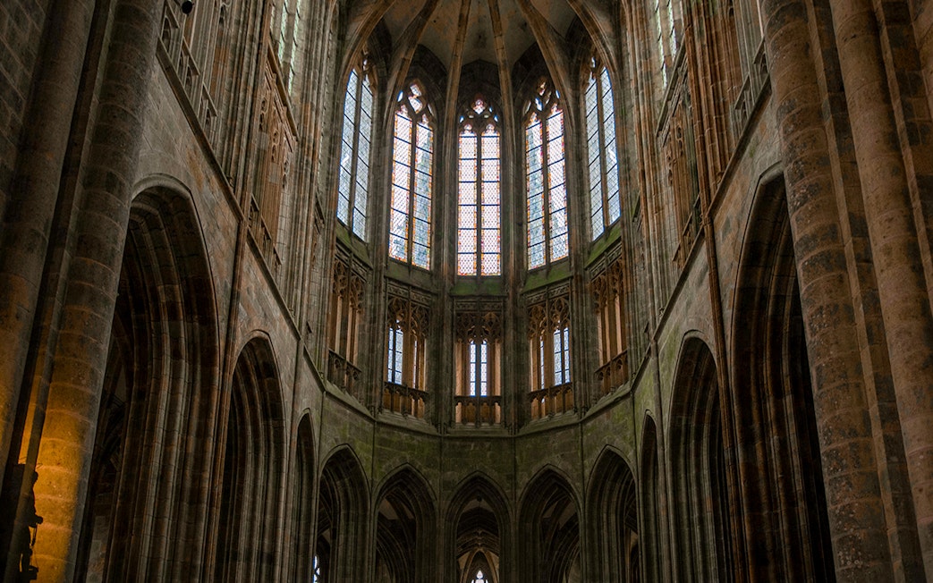 Interior view of Mont Saint Michel Abbey's Gothic arches and stained glass windows in Normandy, France.