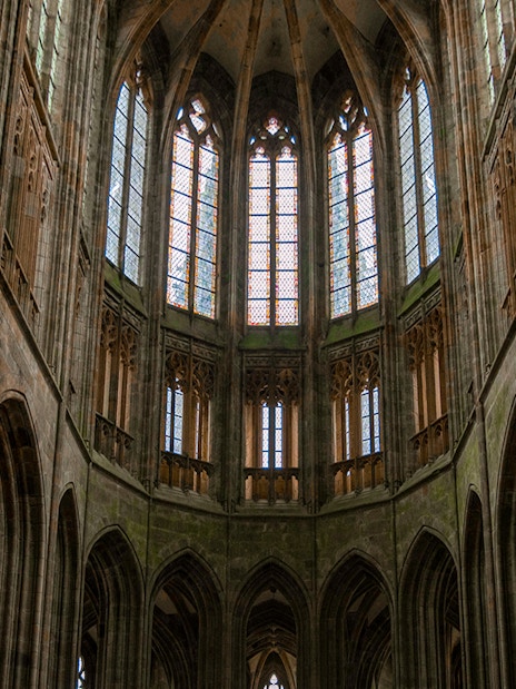 Interior view of Mont Saint Michel Abbey's Gothic arches and stained glass windows in Normandy, France.