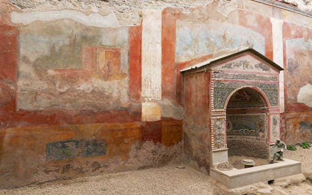 Ancient frescoes and a decorated niche in a Pompeii ruin, part of the daily tour from Naples.