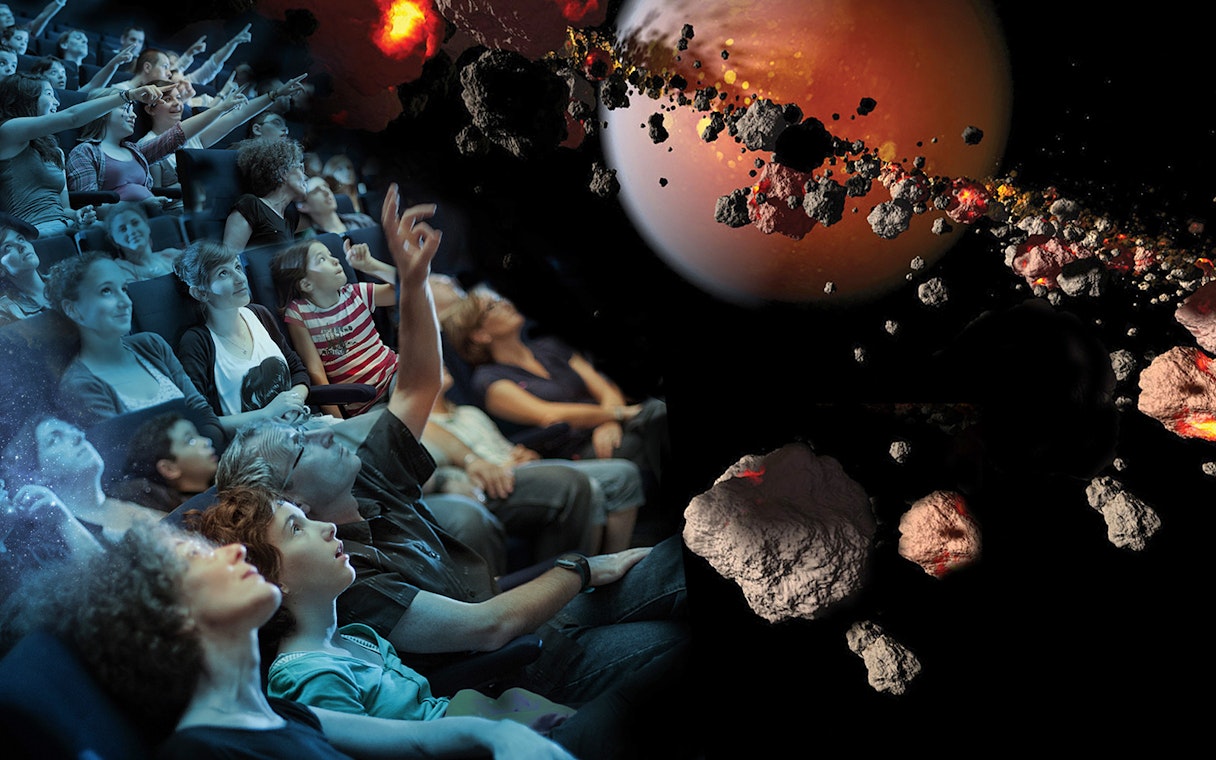Visitors watching a space-themed show at Futuroscope, featuring asteroids and a planet.