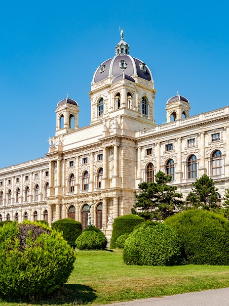 Natural History Museum in Vienna with manicured gardens and blue sky.