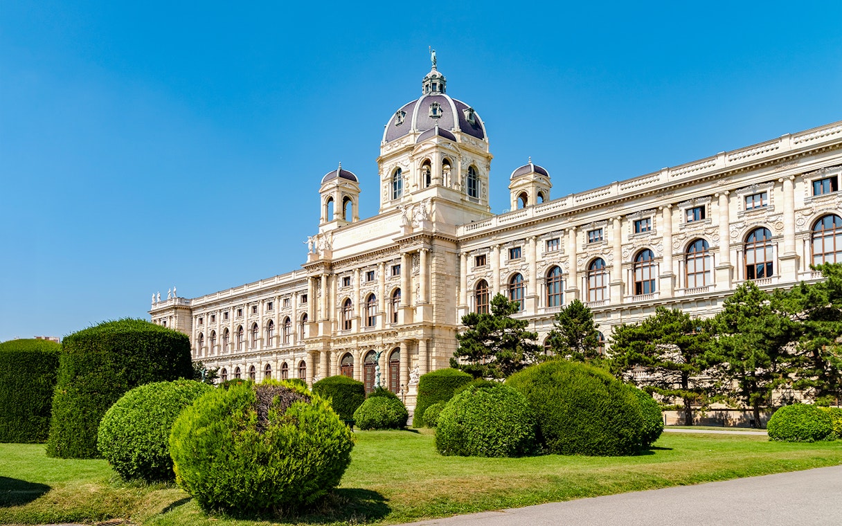 Natural History Museum in Vienna with manicured gardens and blue sky.
