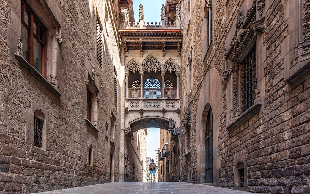 Visitor exploring the Gothic Quarter's narrow street under the Bishop's Bridge in Barcelona.