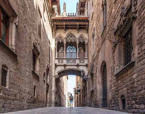 Visitor exploring the Gothic Quarter's narrow street under the Bishop's Bridge in Barcelona.