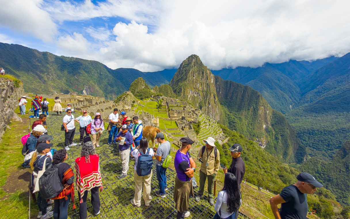 Tourists with guide overlooking Machu Picchu ruins in Peru.