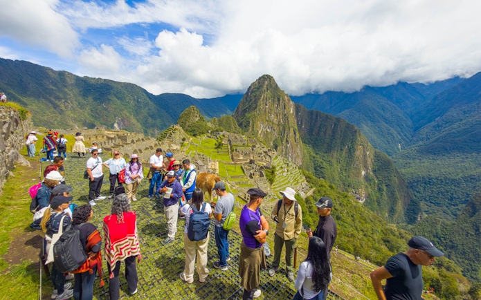 Tourists with guide overlooking Machu Picchu ruins in Peru.