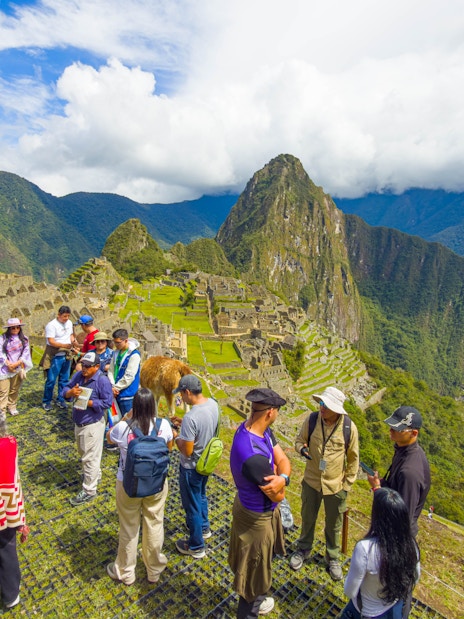 Tourists with guide overlooking Machu Picchu ruins in Peru.