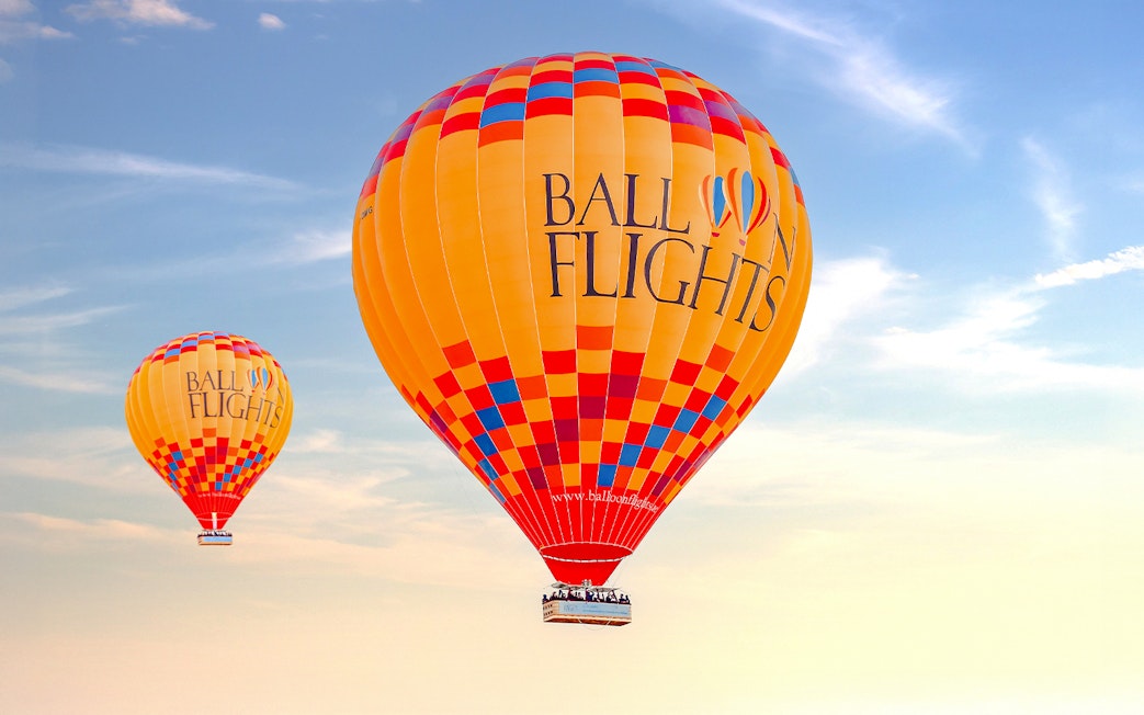 Hot air balloons in flight against a clear sky, part of a tour with hotel transfers and activities.
