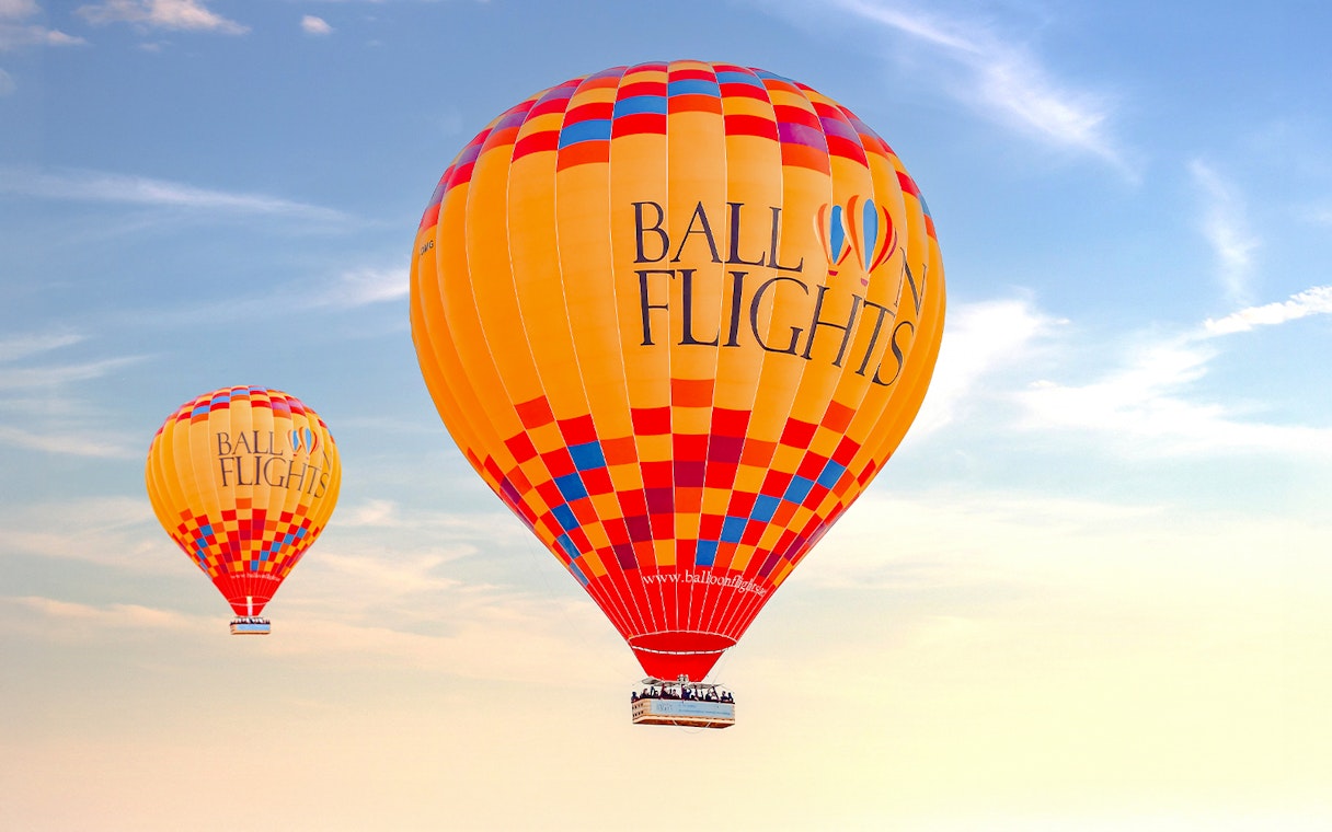 Hot air balloons in flight against a clear sky, part of a tour with hotel transfers and activities.