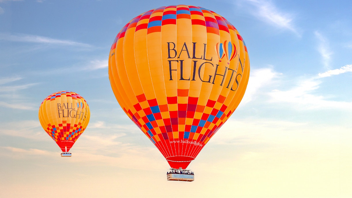 Hot air balloons in flight against a clear sky, part of a tour with hotel transfers and activities.