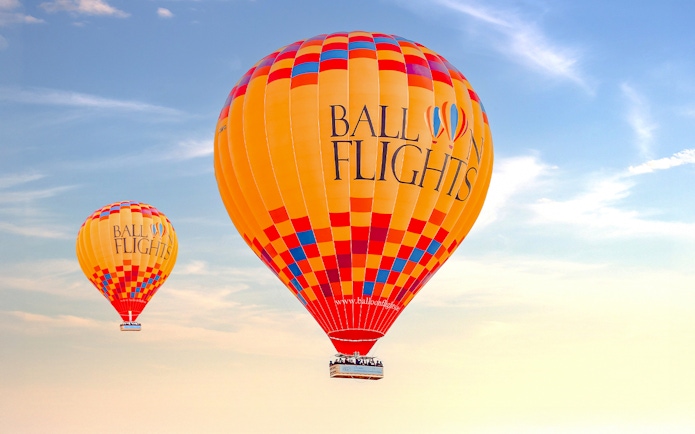 Hot air balloons in flight against a clear sky, part of a tour with hotel transfers and activities.