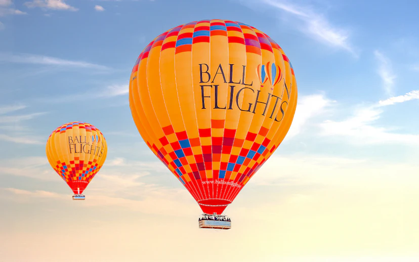 Hot air balloons in flight against a clear sky, part of a tour with hotel transfers and activities.