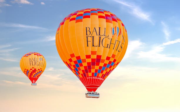 Hot air balloons in flight against a clear sky, part of a tour with hotel transfers and activities.