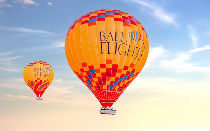Hot air balloons in flight against a clear sky, part of a tour with hotel transfers and activities.