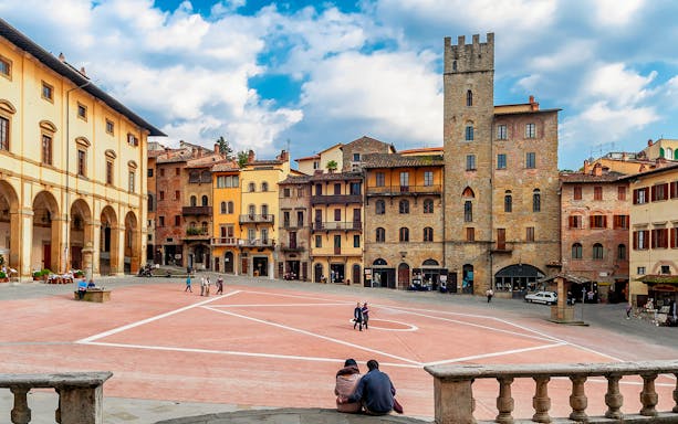 Couple sitting in Piazza Grande, Arezzo, surrounded by historic buildings.