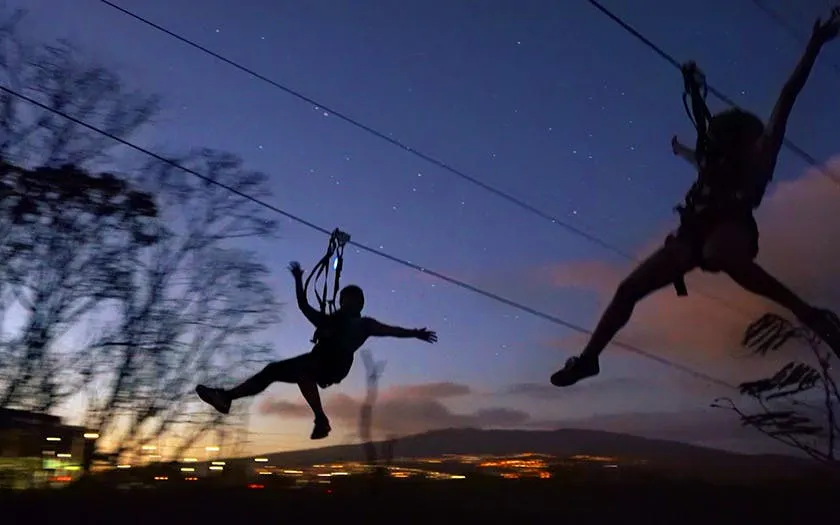 Nighttime ziplining adventure with silhouetted figures against a starry sky.