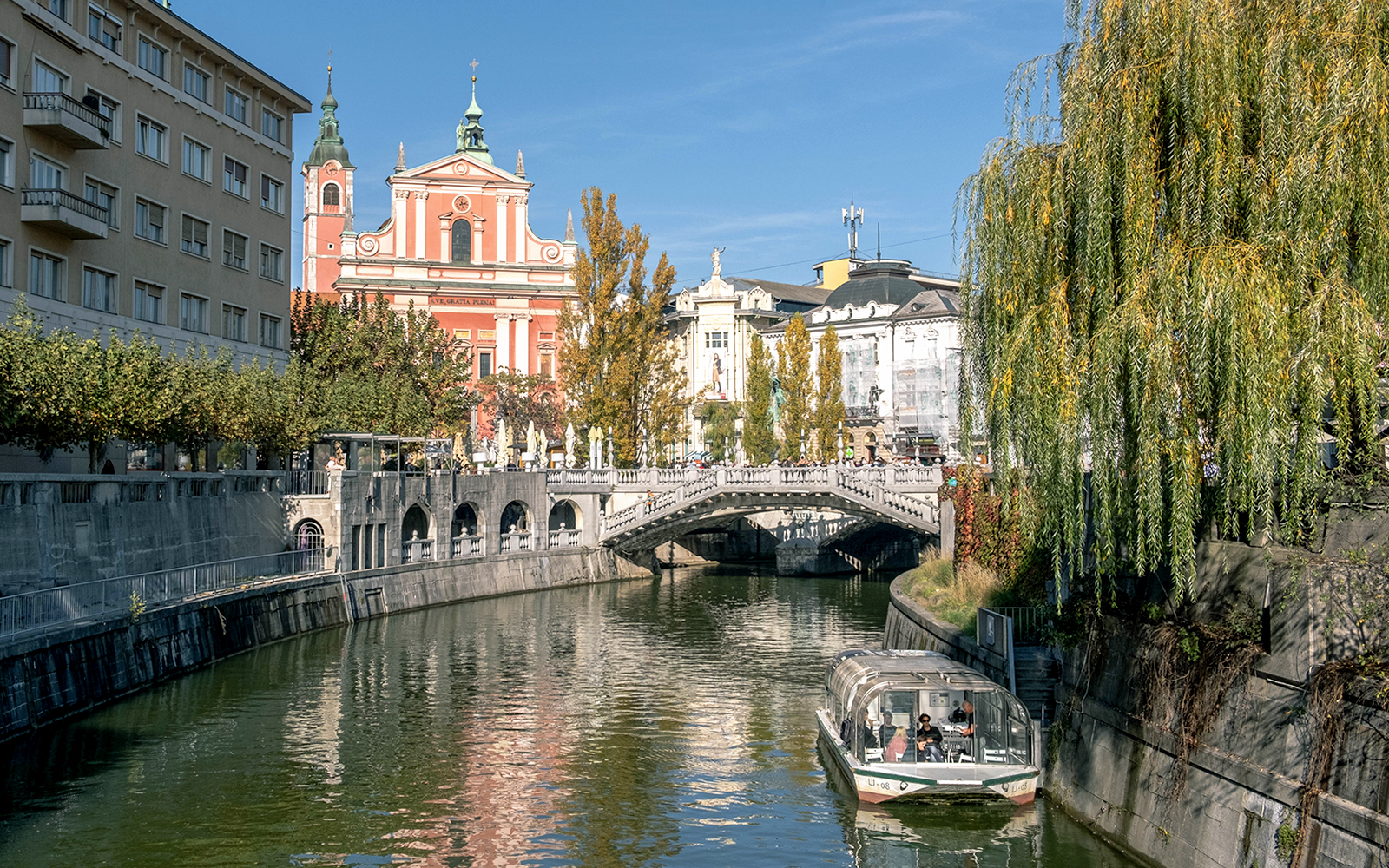 Preseren Square view with triple bridge, river, boat, and Catholic Church of the Annunciation, Ljubljana.