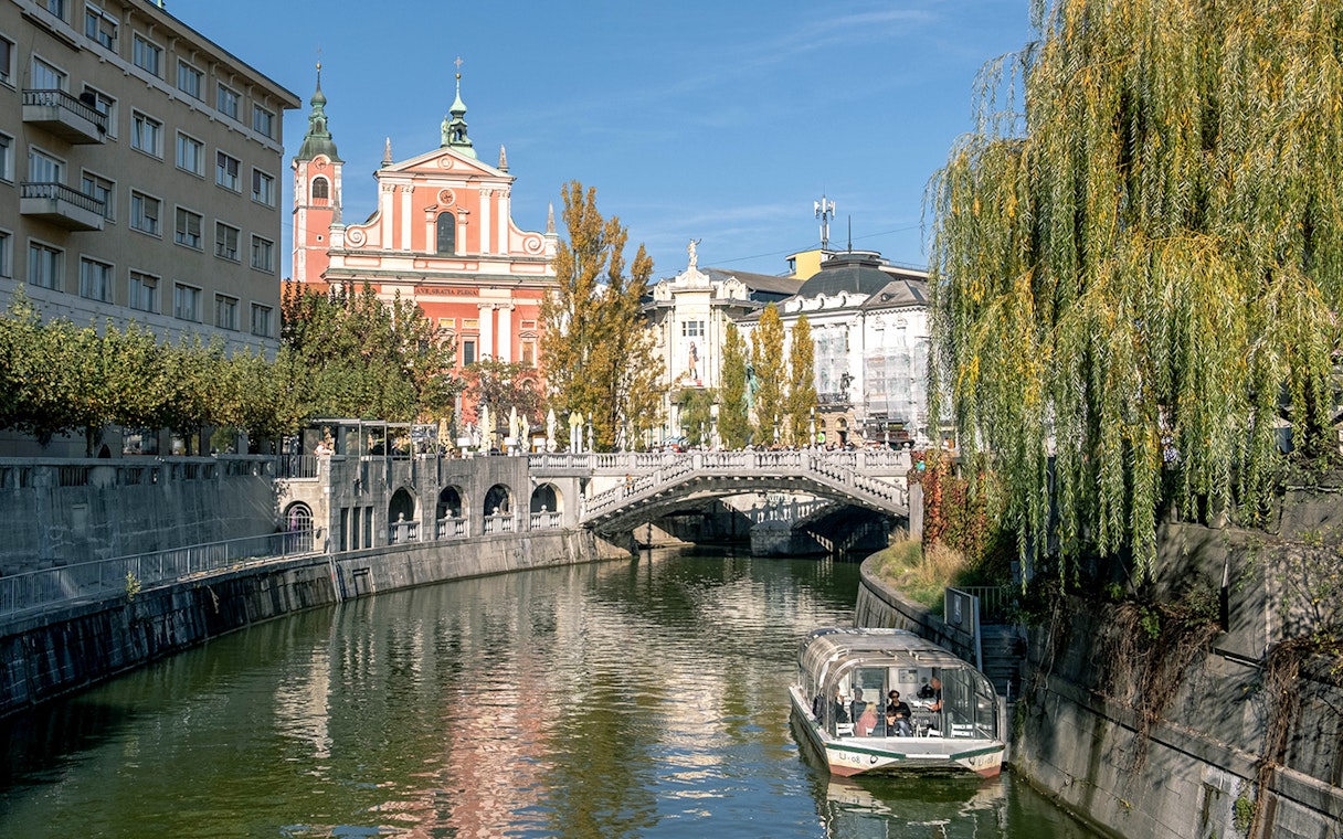 Preseren Square view with triple bridge, river, boat, and Catholic Church of the Annunciation, Ljubljana.
