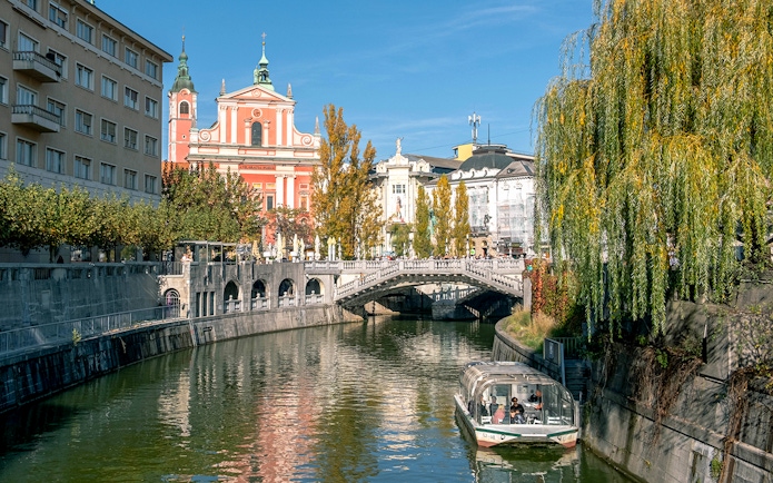 Preseren Square view with triple bridge, river, boat, and Catholic Church of the Annunciation, Ljubljana.