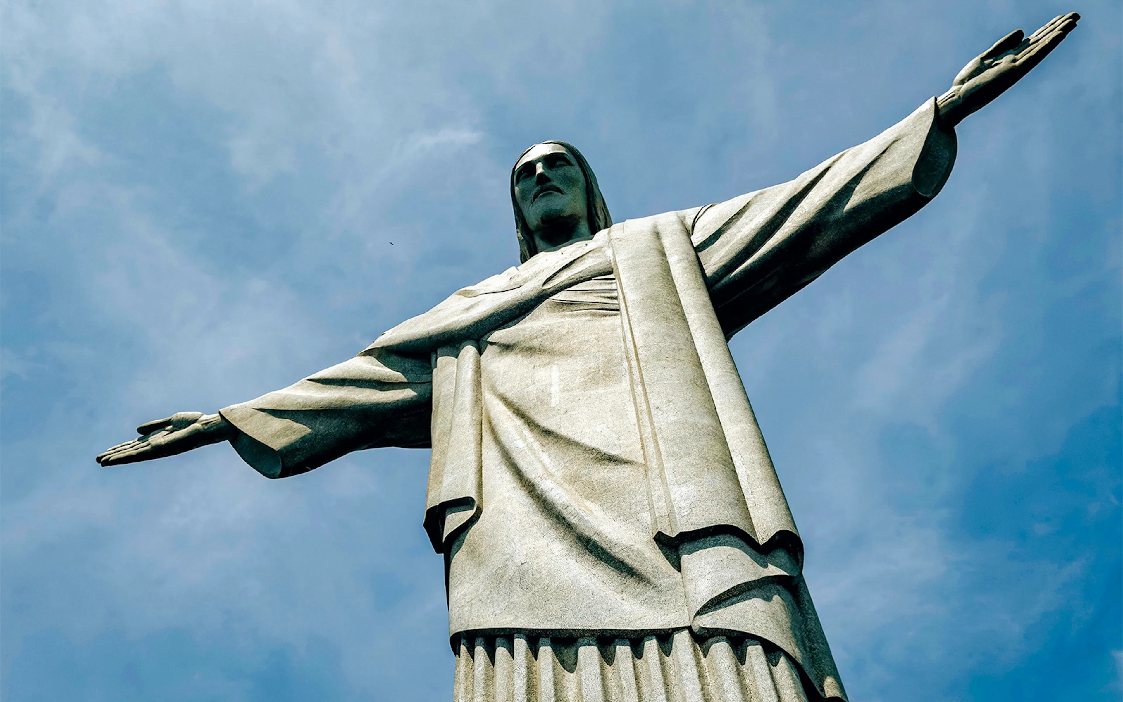 Christ the Redeemer statue with outstretched arms against blue sky, Rio de Janeiro, Brazil.