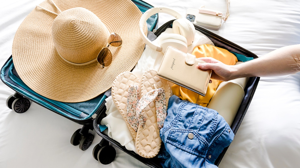 Open suitcase with sun hat, sunglasses, flip-flops, and wallet, essentials for Marseille beach trip.