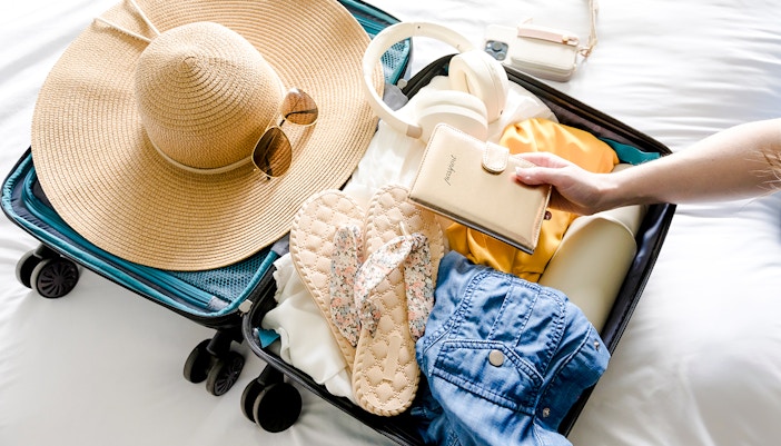 Open suitcase with sun hat, sunglasses, flip-flops, and wallet, essentials for Marseille beach trip.