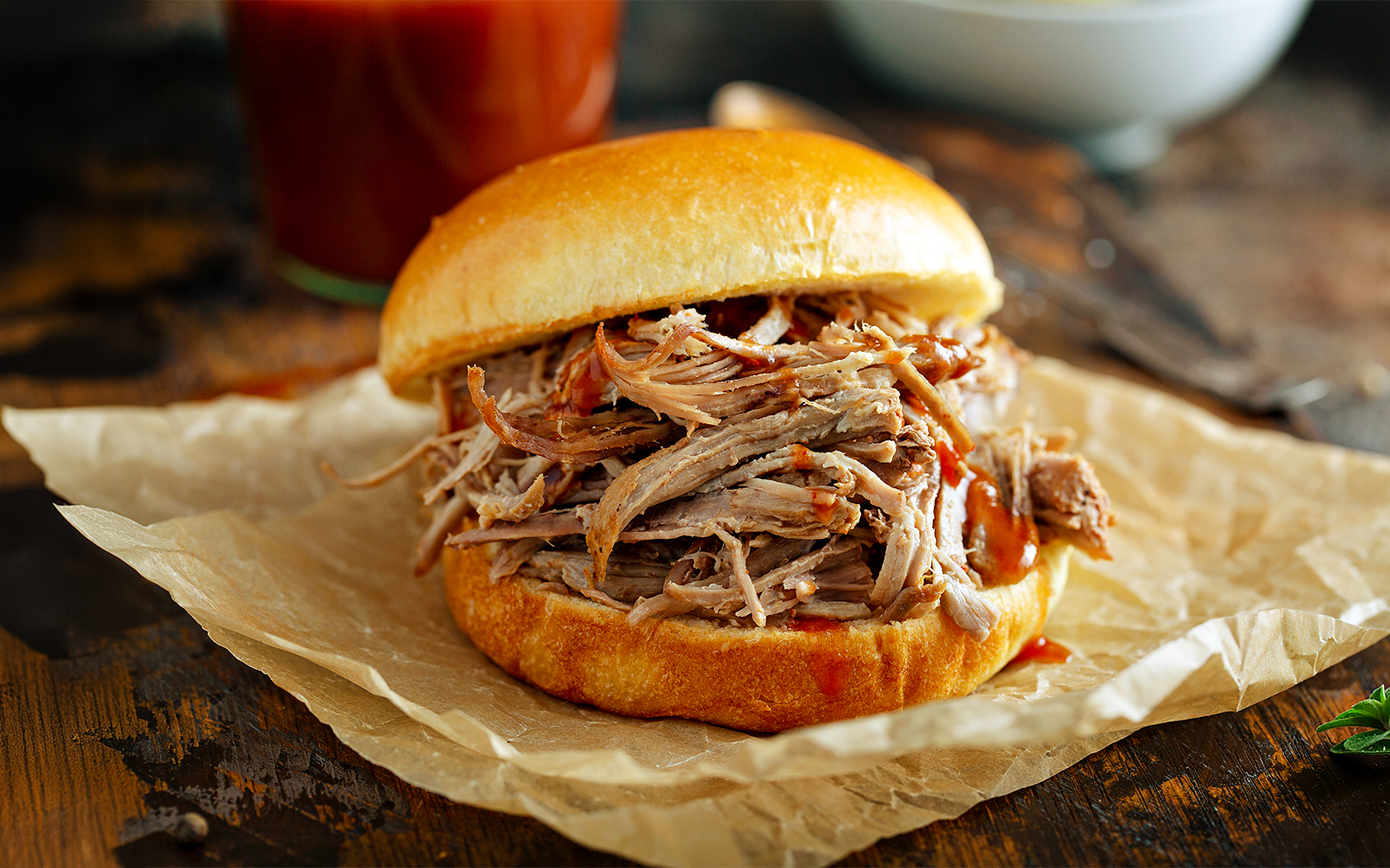 Pulled pork sandwich on parchment paper with barbecue sauce.