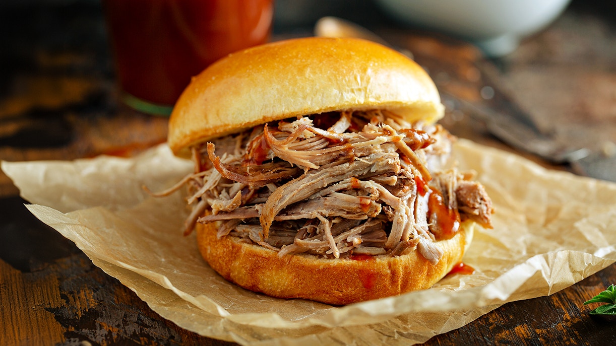 Pulled pork sandwich on parchment paper with barbecue sauce.