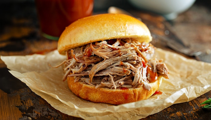 Pulled pork sandwich on parchment paper with barbecue sauce.