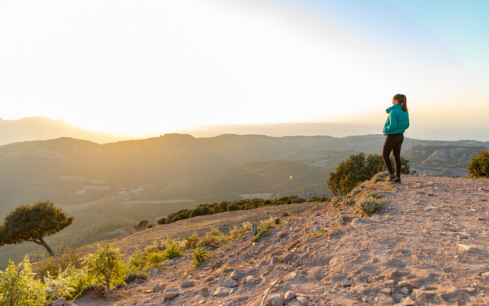 Beautiful woman standing on an edge during sunset with mountains on the background