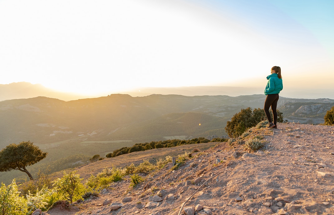 Beautiful woman standing on an edge during sunset with mountains on the background