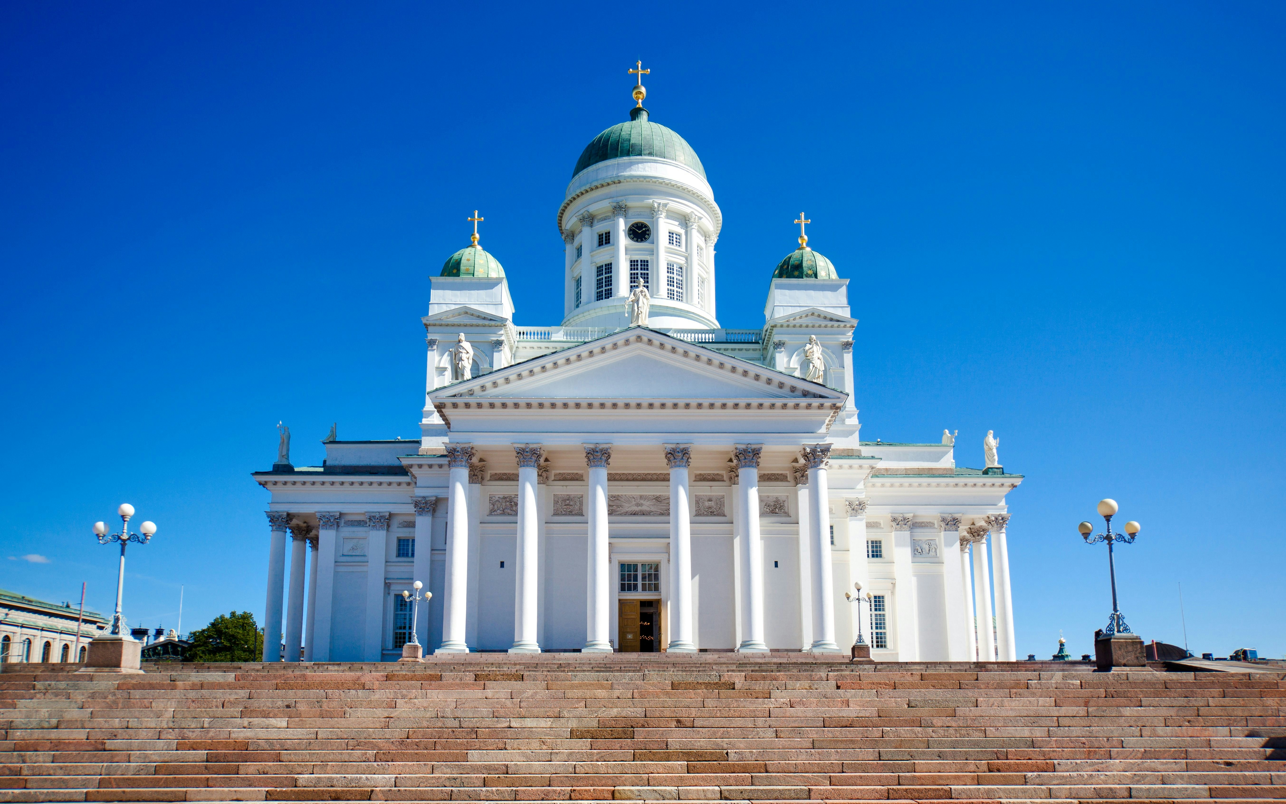 Exterior da Catedral de Helsínquia com degraus e colunas sob um céu azul claro.