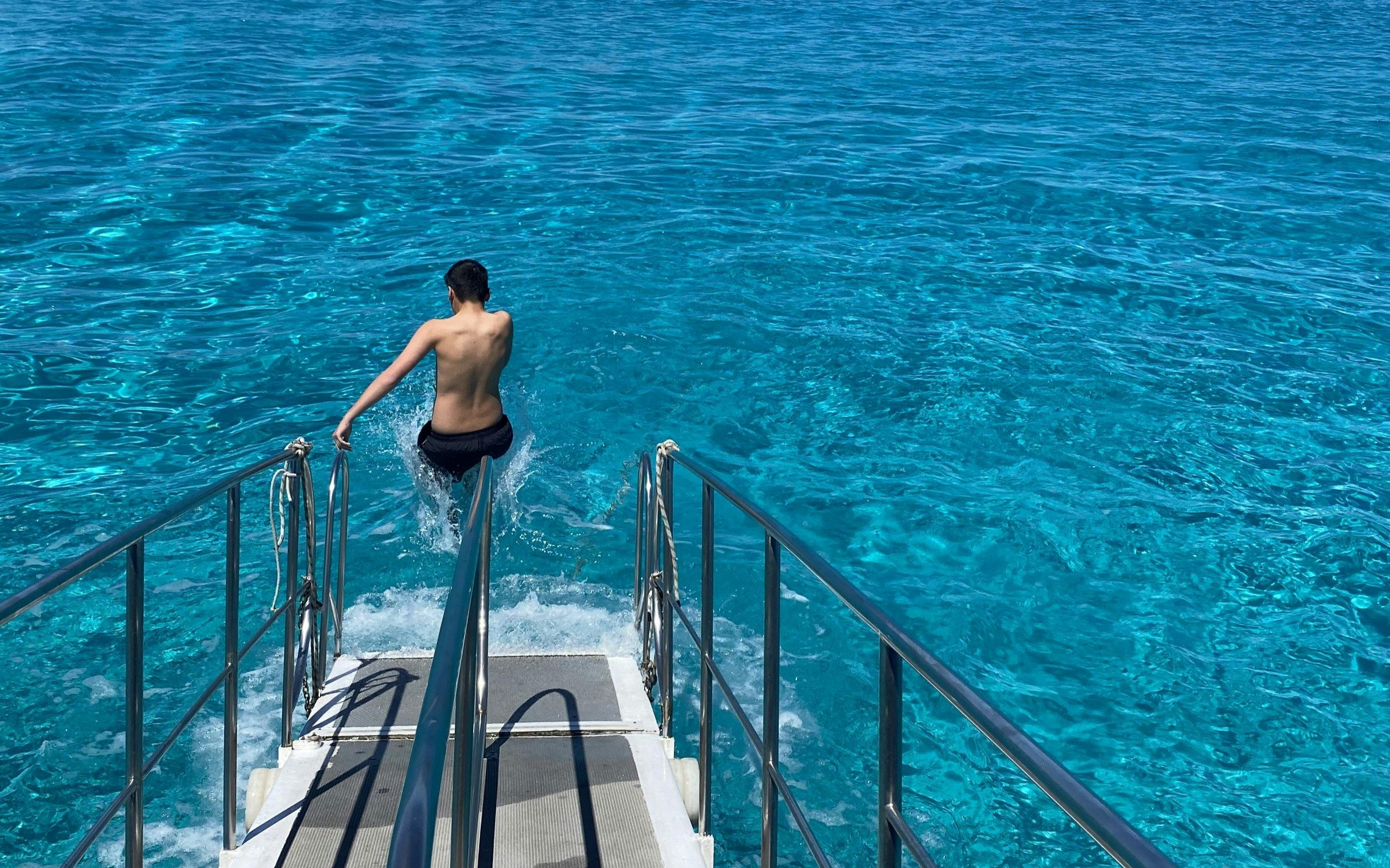 Person jumping into clear blue sea from boat ladder on mini cruise near Favignana.