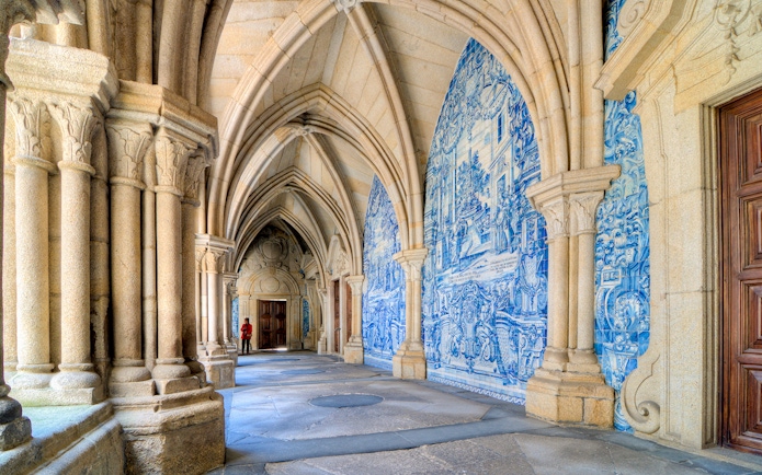 Tourist exploring the cloisters of Porto Cathedral, Portugal, with blue azulejo tiles.