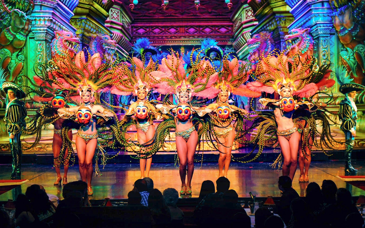 Moulin Rouge Paris dancers performing on stage with vibrant costumes and champagne on table.