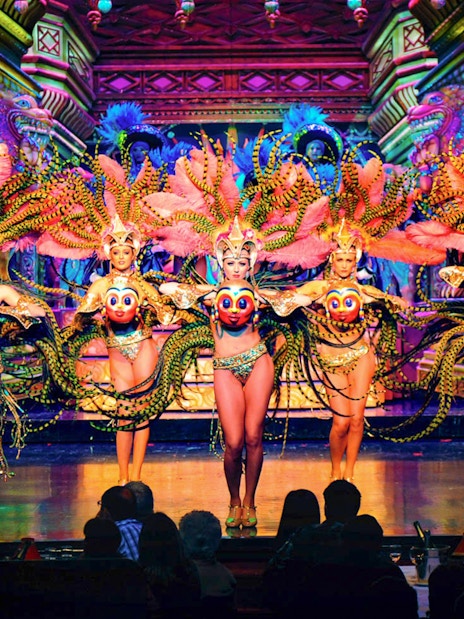 Moulin Rouge Paris dancers performing on stage with vibrant costumes and champagne on table.