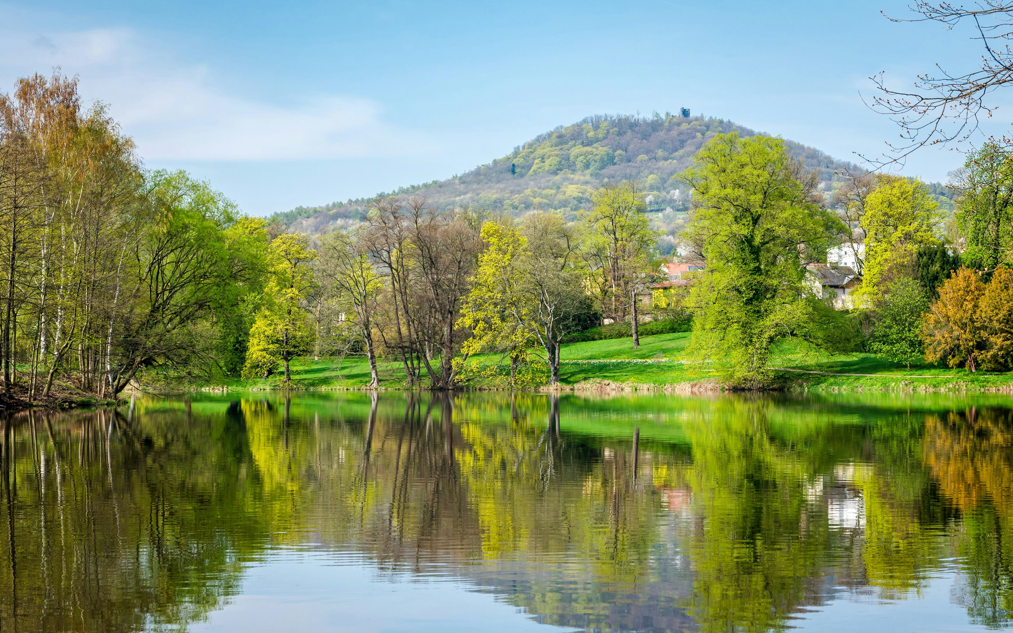 Springtime view of River Ohře with lush trees and a hill in the background.