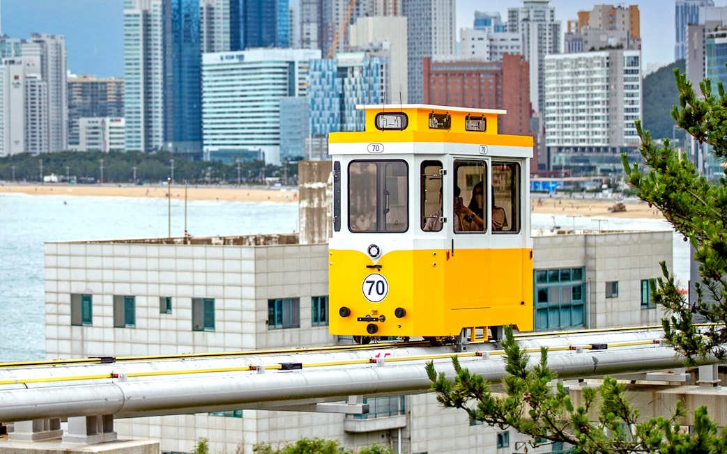 Yellow sky capsule on track with Busan cityscape in background.